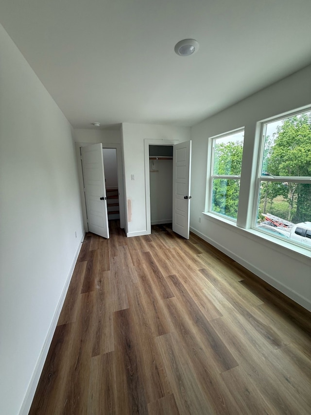 unfurnished bedroom featuring baseboards, wood finished floors, and a closet