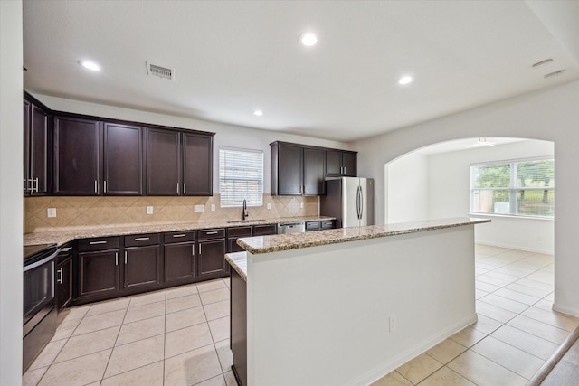 22702 Crate Falls Dr, Hockley, TX 77447 - kitchen featuring a kitchen island, arched walkways, a sink, a wealth of natural light, and stainless steel appliances