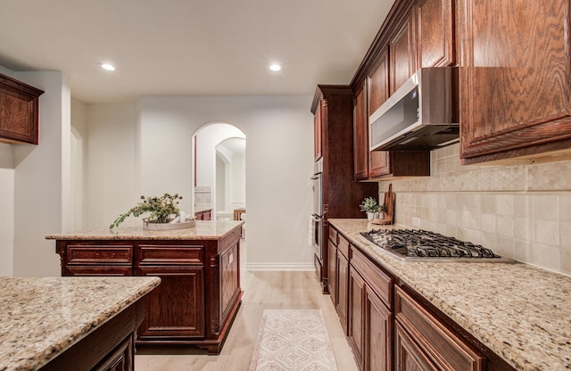 1840 Leela Springs Dr, Conroe, TX 77304 - kitchen featuring arched walkways, light wood finished floors, backsplash, appliances with stainless steel finishes, and light stone countertops