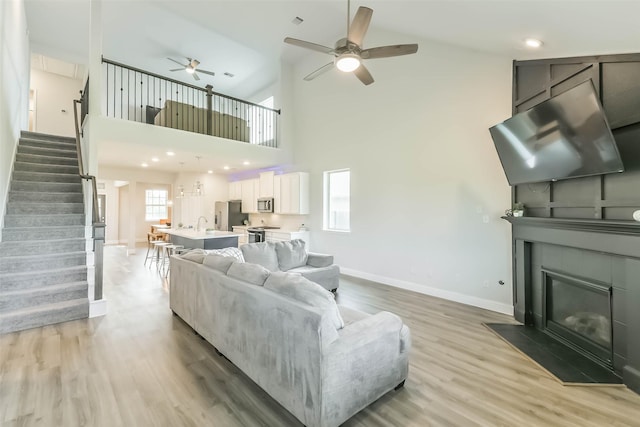 living area featuring light wood finished floors, baseboards, a ceiling fan, stairs, and a fireplace