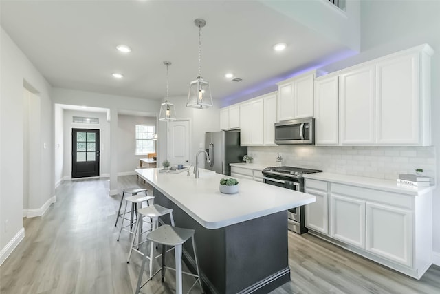 kitchen with stainless steel appliances, light wood-style flooring, decorative backsplash, and a center island with sink