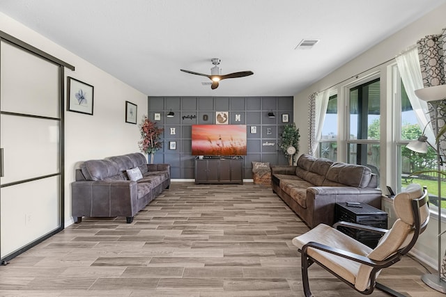 living area featuring light wood-style floors, plenty of natural light, visible vents, and a ceiling fan