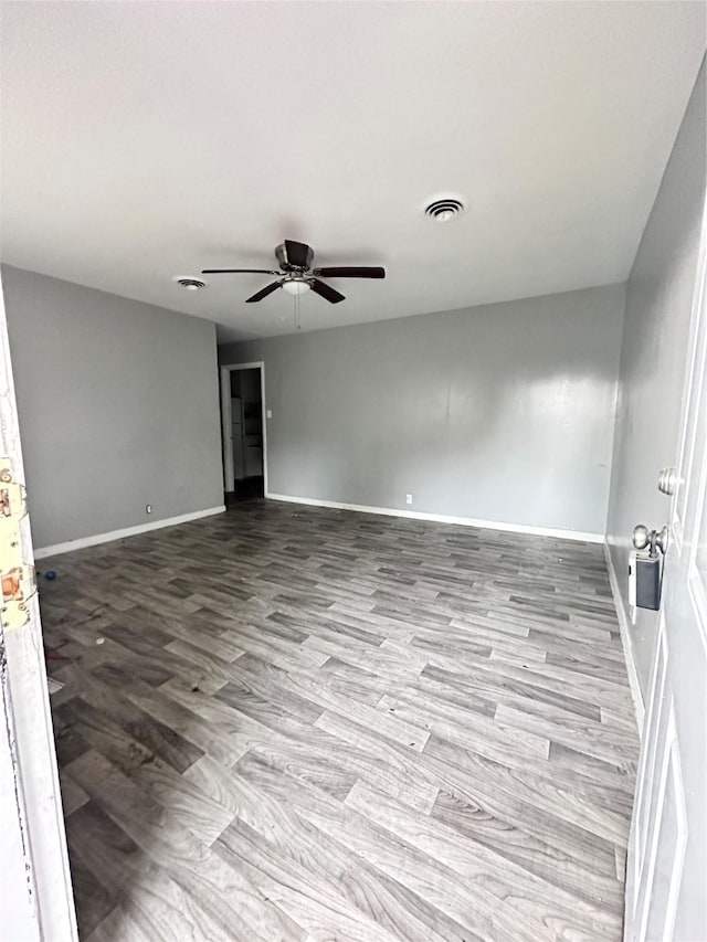 spare room with wood finished floors, baseboards, a ceiling fan, and visible vents