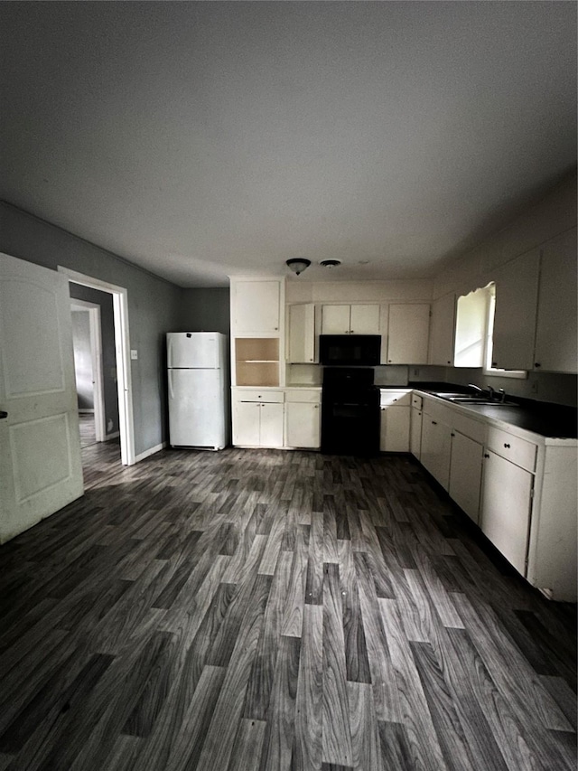 kitchen featuring a sink, dark wood-style flooring, freestanding refrigerator, white cabinetry, and black microwave