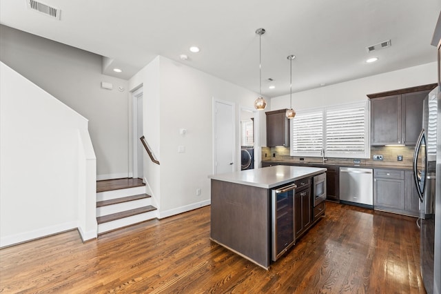 kitchen with beverage cooler, washer / dryer, appliances with stainless steel finishes, and visible vents