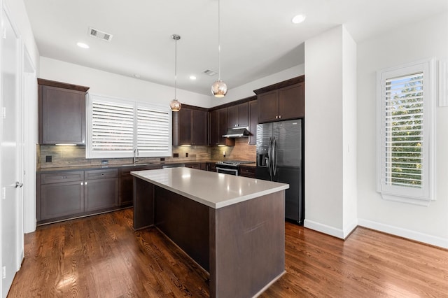 kitchen with stainless steel range, dark brown cabinetry, under cabinet range hood, refrigerator with ice dispenser, and visible vents
