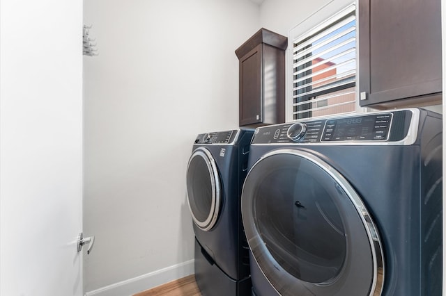 laundry area featuring separate washer and dryer, cabinet space, baseboards, and wood finished floors