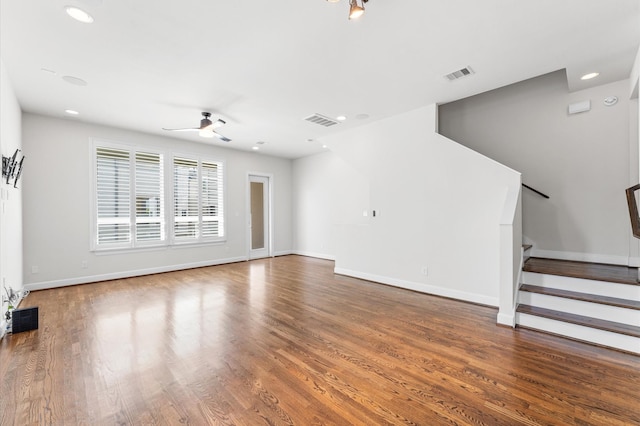 unfurnished living room featuring baseboards, visible vents, wood finished floors, and stairway
