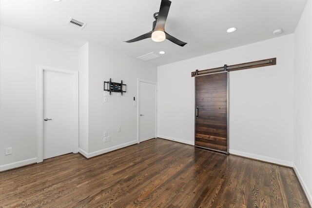 unfurnished bedroom featuring wood finished floors, baseboards, a barn door, and visible vents