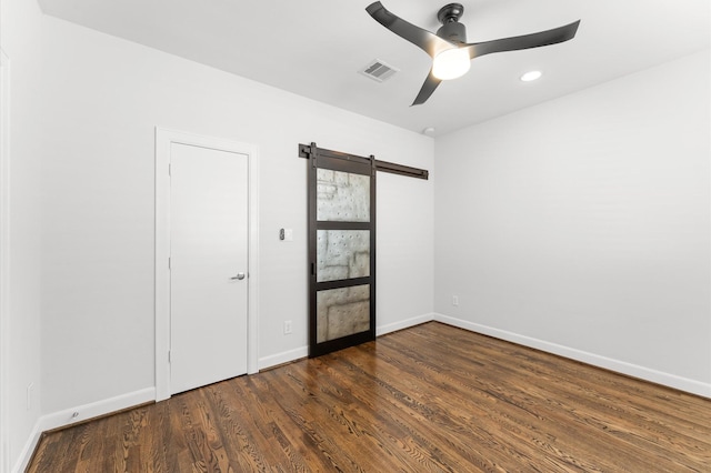 empty room with ceiling fan, visible vents, wood finished floors, a barn door, and baseboards