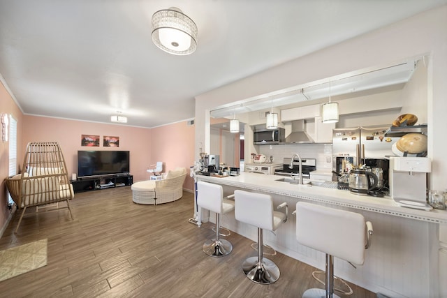 8931 Gaylord St Unit 161, Houston, TX 77024 - kitchen with wall chimney exhaust hood, stainless steel appliances, a kitchen breakfast bar, decorative backsplash, and wood finished floors
