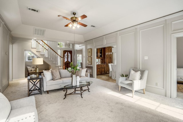 living room featuring light colored carpet, a ceiling fan, stairs, and visible vents