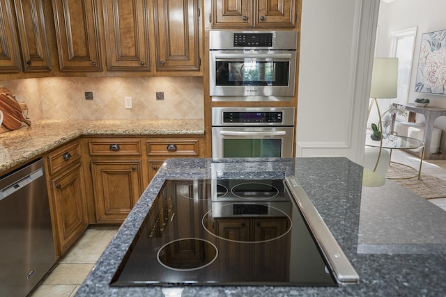 kitchen with brown cabinetry, decorative backsplash, dark stone countertops, and stainless steel appliances