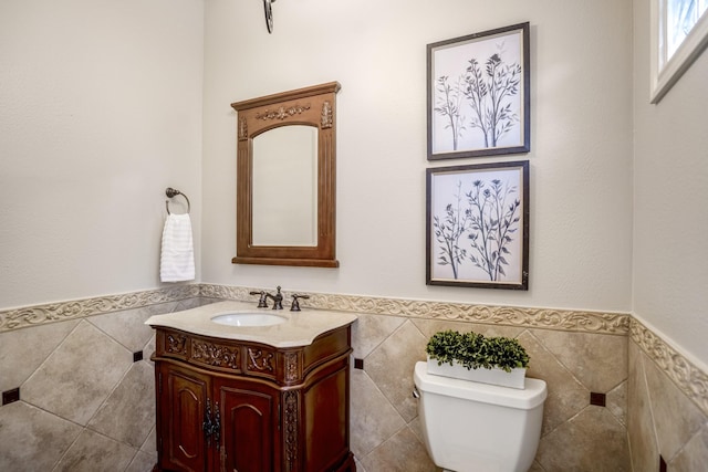 bathroom with vanity, a wainscoted wall, toilet, and tile walls