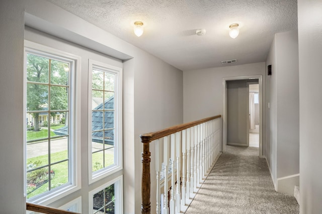 corridor with baseboards, light carpet, a textured ceiling, and visible vents