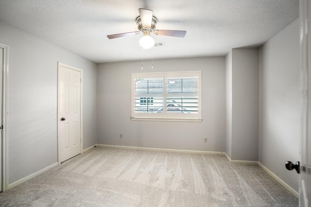 empty room with light colored carpet, a ceiling fan, a textured ceiling, and baseboards