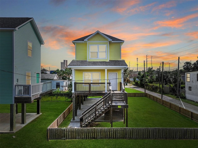 back of house at dusk with stairs, a fenced backyard, a yard, a patio, and roof with shingles