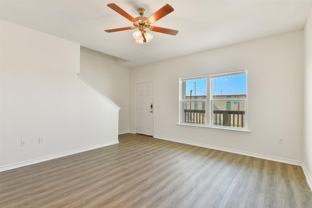 spare room with wood finished floors, a ceiling fan, and baseboards