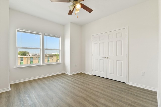 unfurnished bedroom featuring ceiling fan, baseboards, wood finished floors, and a closet