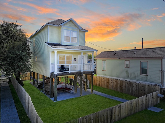 1302 55th St, Galveston, TX 77551 - back of property at dusk featuring a patio area, a lawn, a fenced backyard, roof with shingles, and stairs