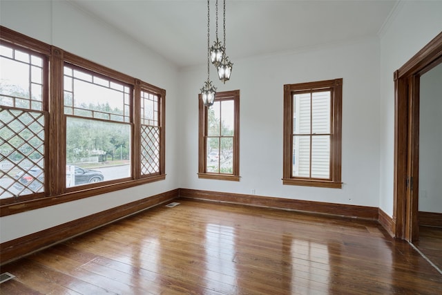 unfurnished dining area with hardwood / wood-style floors, baseboards, ornamental molding, and visible vents