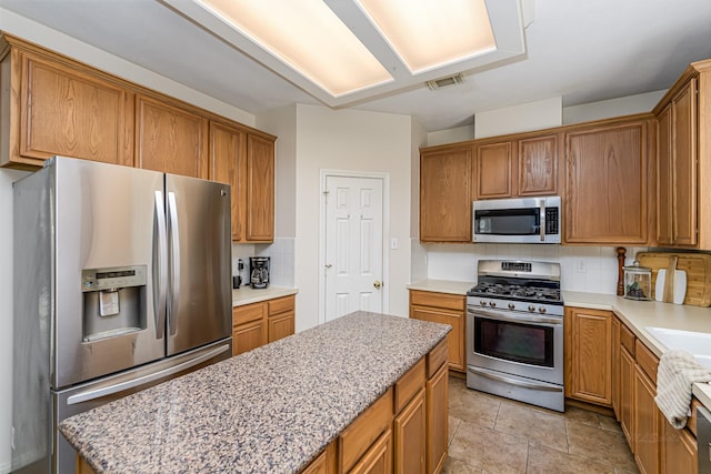 6249 Mallard Dr, Katy, TX 77493 - kitchen featuring a center island, tasteful backsplash, brown cabinets, appliances with stainless steel finishes, and visible vents