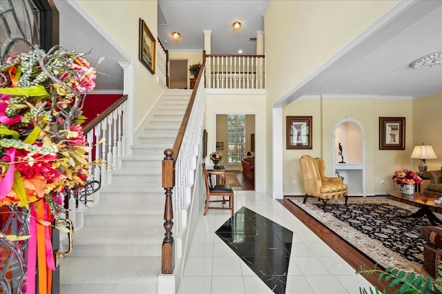 tiled entrance foyer featuring stairway, a high ceiling, crown molding, and baseboards