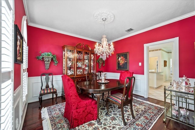 dining space with visible vents, crown molding, a chandelier, and wainscoting