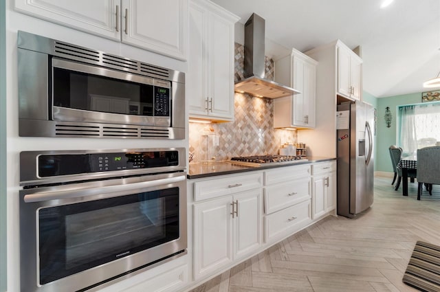 kitchen with stainless steel appliances, backsplash, dark countertops, wall chimney range hood, and white cabinetry