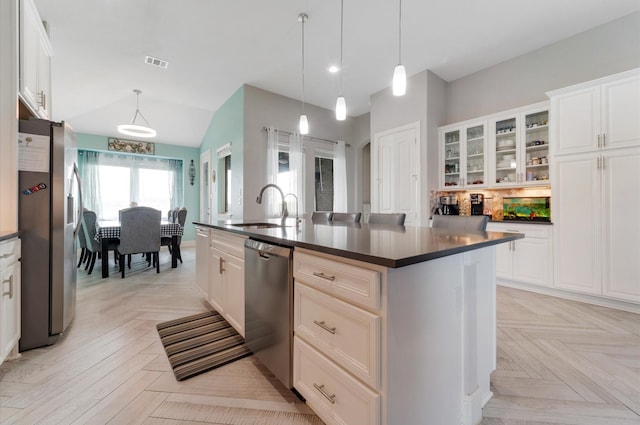 kitchen featuring dark countertops, a sink, a kitchen island with sink, appliances with stainless steel finishes, and visible vents