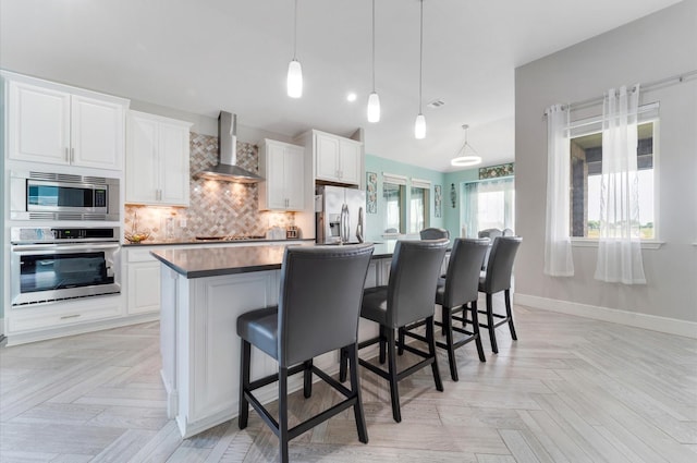 kitchen featuring backsplash, wall chimney exhaust hood, appliances with stainless steel finishes, and white cabinetry