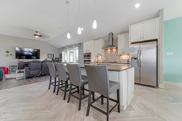 kitchen featuring lofted ceiling, wall chimney range hood, a kitchen breakfast bar, and stainless steel appliances