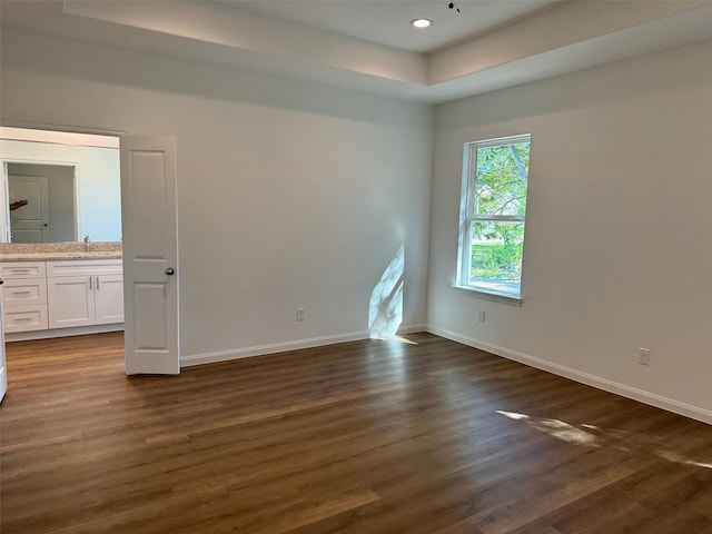 unfurnished bedroom with a sink, a tray ceiling, baseboards, dark wood-style floors, and recessed lighting