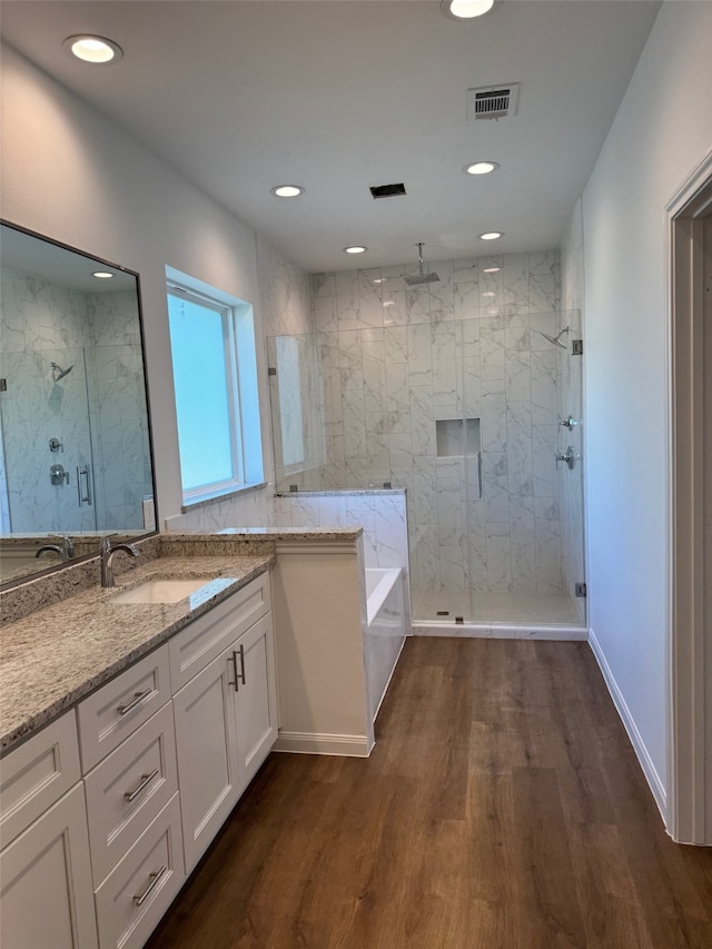 bathroom featuring wood finished floors, visible vents, vanity, a bath, and a stall shower
