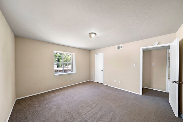 empty room featuring a textured ceiling, dark carpet, visible vents, and baseboards