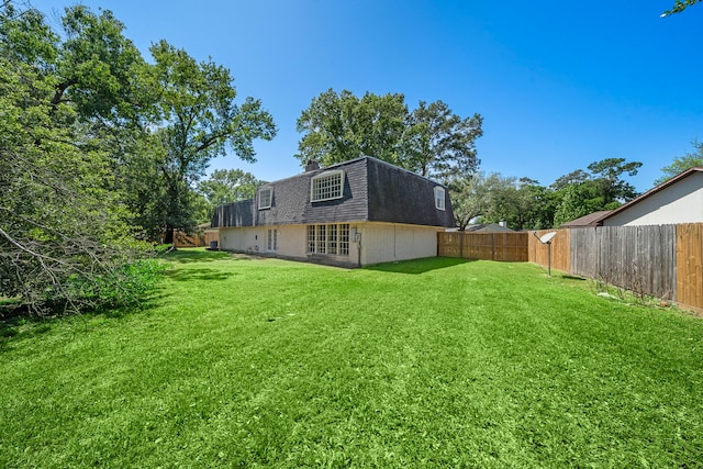 rear view of house featuring a yard, roof with shingles, a fenced backyard, and mansard roof