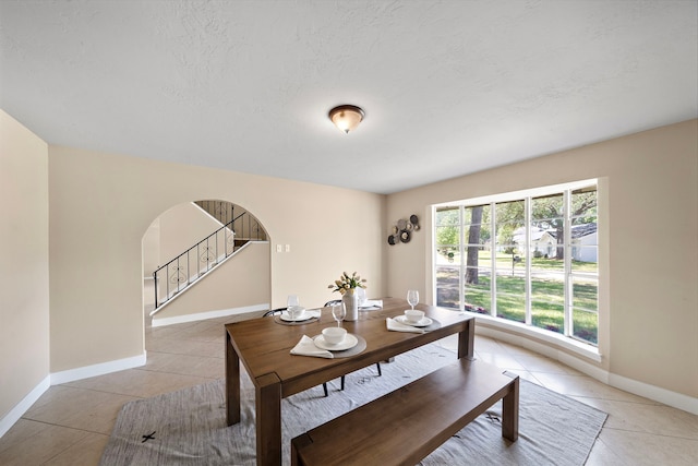 dining space featuring baseboards, arched walkways, stairs, and light tile patterned floors