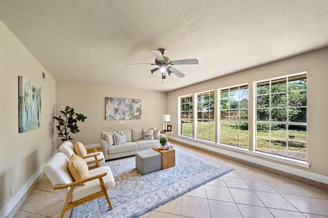 living area featuring light tile patterned floors, baseboards, a textured ceiling, and ceiling fan