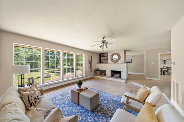 living area with light tile patterned floors, ceiling fan, baseboards, a brick fireplace, and visible vents