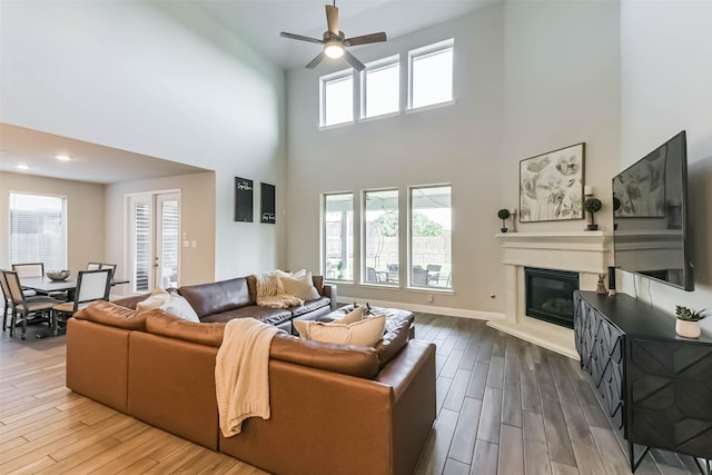 19219 Filly Park Cir, Tomball, TX 77377 - living area featuring dark wood finished floors, ceiling fan, a glass covered fireplace, a towering ceiling, and baseboards