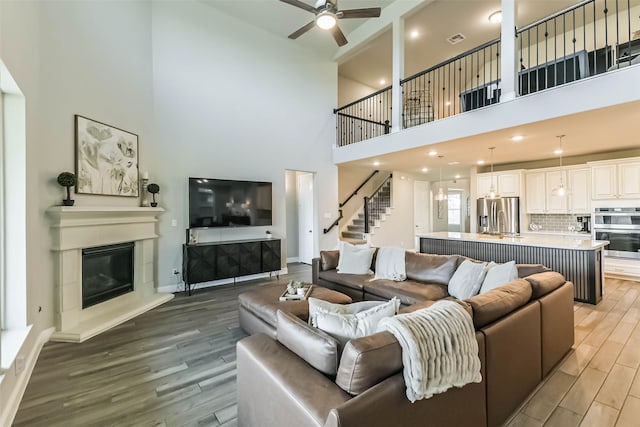 19219 Filly Park Cir, Tomball, TX 77377 - living area with a high ceiling, light wood-style flooring, a ceiling fan, a glass covered fireplace, and stairs