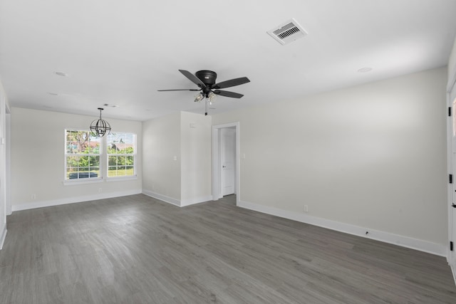 spare room with ceiling fan with notable chandelier, baseboards, visible vents, and dark wood finished floors