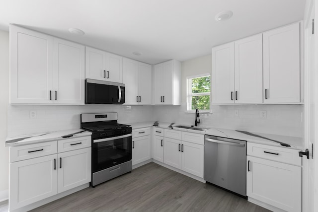 kitchen with stainless steel appliances, backsplash, a sink, light wood-type flooring, and white cabinetry