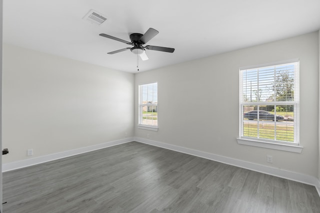 empty room with baseboards, visible vents, a ceiling fan, and dark wood-style floors