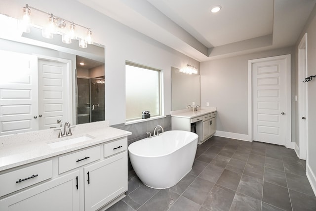 bathroom with two vanities, a sink, a freestanding bath, a stall shower, and baseboards