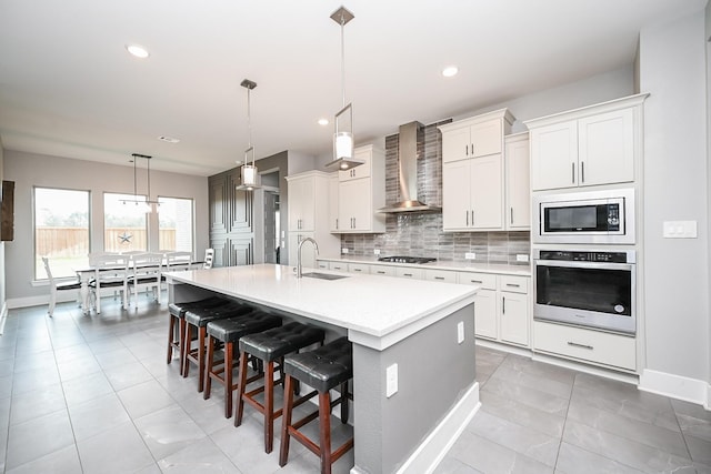 kitchen with wall chimney range hood, a sink, light countertops, backsplash, and appliances with stainless steel finishes