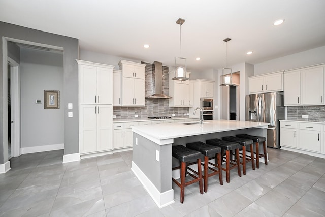 kitchen featuring a sink, decorative backsplash, light countertops, wall chimney exhaust hood, and appliances with stainless steel finishes