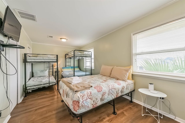 bedroom with wood finished floors, visible vents, and crown molding