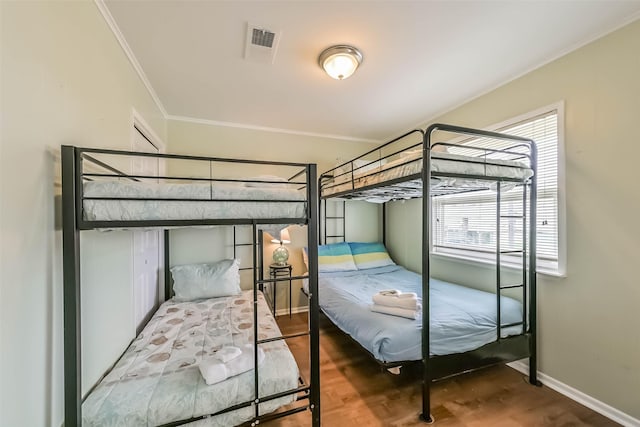bedroom featuring wood finished floors, visible vents, ornamental molding, and multiple windows