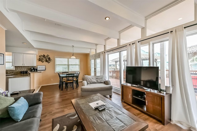living room featuring light wood-type flooring, plenty of natural light, baseboards, and beam ceiling